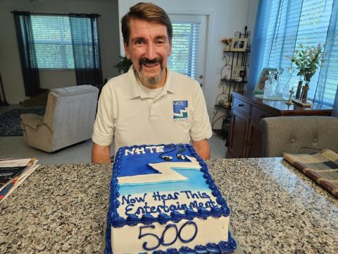 Bruce Wawrzyniak sitting with cake with NHTE logo and 500 on it