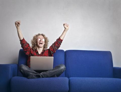 Female with laptop cross-legged on couch with arms raised in jubilation