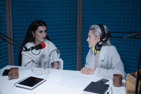 Two girls wearing headphones and sitting at microphones in a padded studio