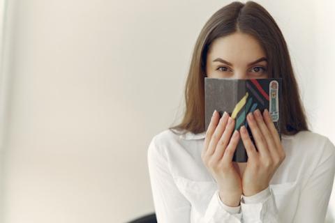 Girl with secretive look holding small book up to cover her mouth