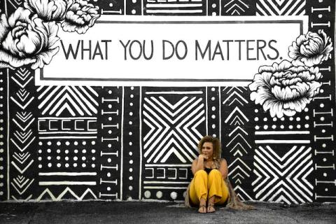 Woman sitting on the ground in front of a What You Do Matters mural