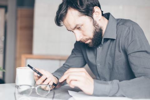 Man sitting down stares with confusion at smartphone