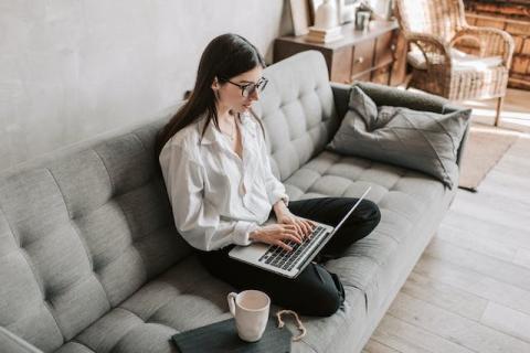 Girl typing on laptop while sitting cross-legged on couch