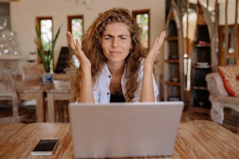 Seated at table girl with long curly hair raises hands in frustration looking at laptop