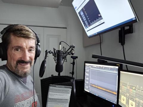 Wearing headphones Bruce Wawrzyniak stands at the microphone in his studio