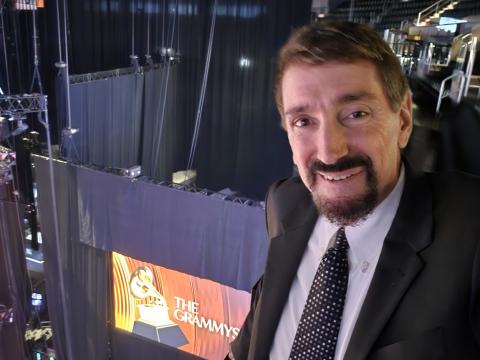 Bruce Wawrzyniak stands inside the Crypto.com Arena flanked by a digital sign for the GRAMMYs