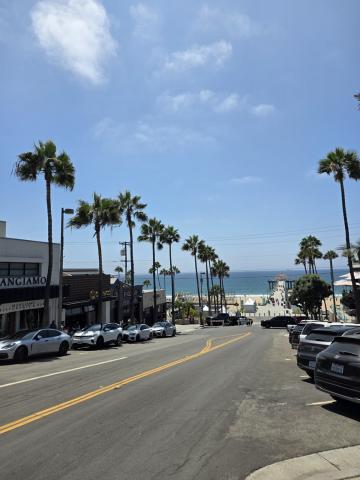Palm trees and parked cars on either side of the street leading down to the Manhattan Beach pier