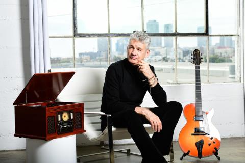Chris Standring sits alongside his guitar in front of a window