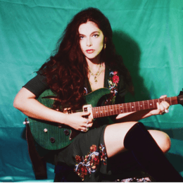 Lola Aviva seated and holding her electric guitar