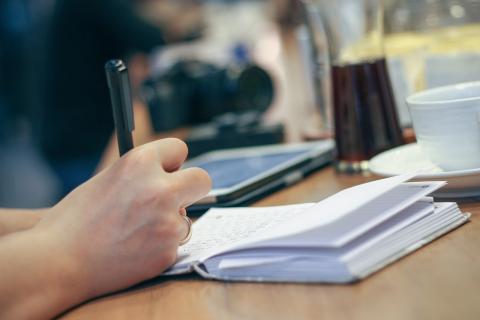 A hand writes with a pen into an open notebook on a table