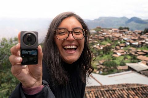 Girl with glasses smiling big outdoors while holding up camera showing photo