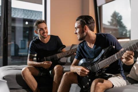 Two young men holding guitars seated next to each other on a couch