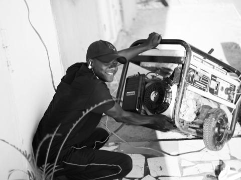 A Black male squatted down working with a generator