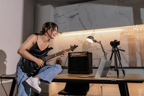 Girl holding electric guitar looking at camera and laptop