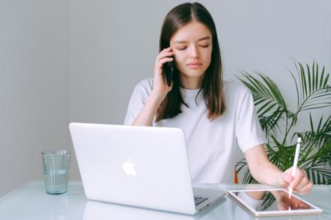 Girl at laptop talking on phone while handwriting notes