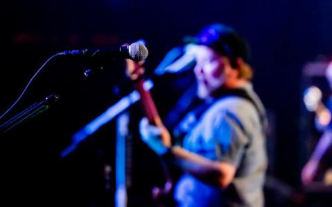 Profile of male on stage at a microphone playing guitar