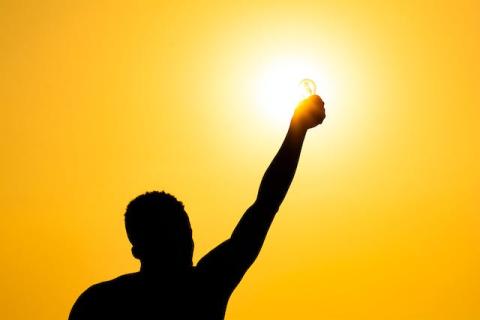 Silhouette of male from behind holding up illuminated light bulb