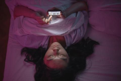 Asian girl laying in bed on her back looking at her smartphone