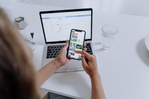 Shot from behind of person looking at smartphone held in front of laptop screen