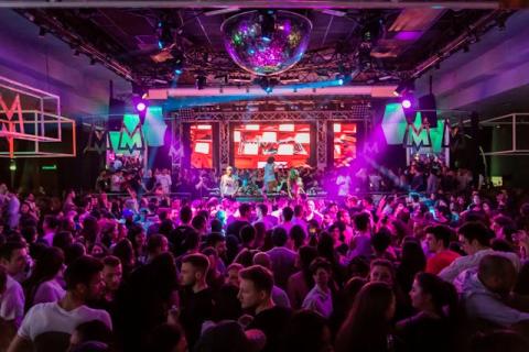 A wide shot of a band on stage playing inside a crowded music club