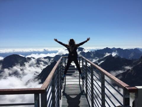 Female with arms raised up high at a mountainous lookout point