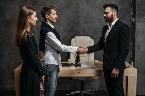 Two men shake hands while a woman stands alongside one of them