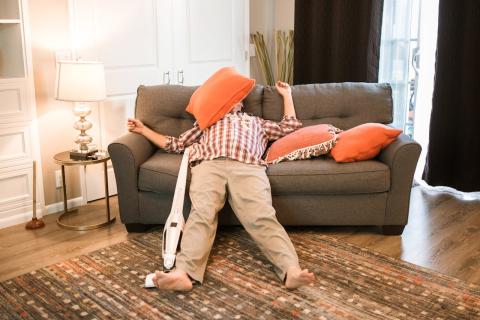 A guy has a face over his pillow as he sprawls out with torso on the couch and lower body on the floor