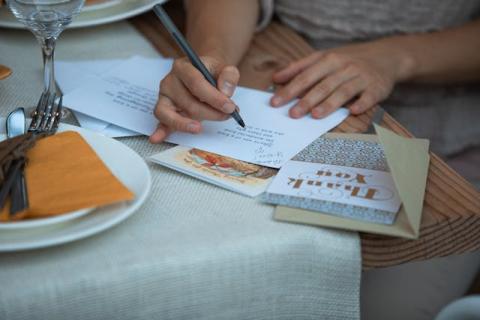 Hands writing out a Thank You greeting card on a table