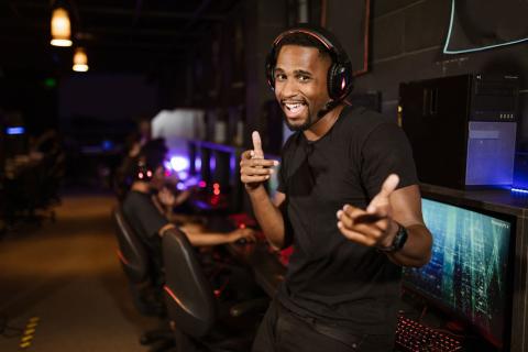 A 30-something Black male wearing a headset has an excited expression and strikes a complementary pose