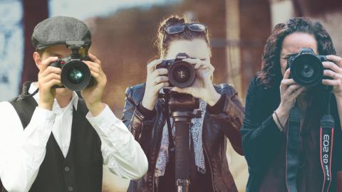 Three photographers stand shoulder to shoulder with their cameras in front of their face resembling paparazzi