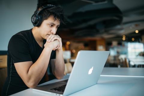 Male seated wearing headphones looking frustratedly at laptop